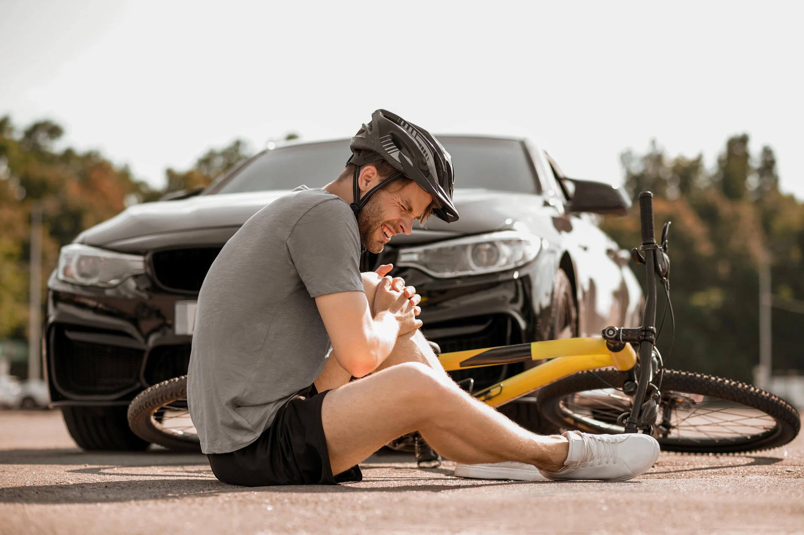 misfortune unhappy guy helmet sitting with closed eyes holding his knee near bicycle road fron car
